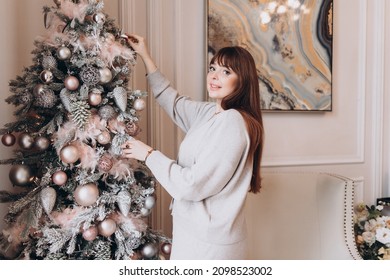 Young Beautiful Woman Plus Size Model In White Knitted Casual Sweater  In Living Room Decorating Christmas Tree, Christmas And New Year Concept