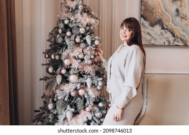 Young Beautiful Woman Plus Size Model In White Knitted Casual Sweater  In Living Room Decorating Christmas Tree, Christmas And New Year Concept