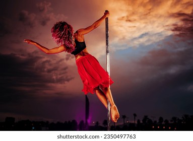 Young beautiful woman pole dancing on twilight sky and city silhouettes background - Powered by Shutterstock