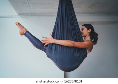 Young beautiful woman practicing aerial different inversion anti-gravity yoga with a hammock in a white modern studio. Concept of a mental and physical health, harmony living