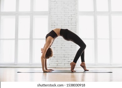 Young beautiful woman practicing yoga near floor window in yoga studio, standing in Bridge exercise, Urdhva Dhanurasana pose. Harmony, balance, relaxation, healthy lifestyle concept