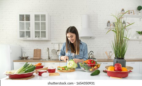 A young beautiful woman is preparing a salad of various vegetables in the kitchen. The concept of a healthy diet and lifestyle.