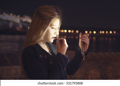 Young Beautiful Woman Putting Makeup and Looking at Himself on Smart Phone. Glow Bokeh Night City Lights in the Background. - Shutterstock ID 531795808