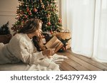 Young beautiful woman reading book, lying near Christmas tree in a cozy decorated room.