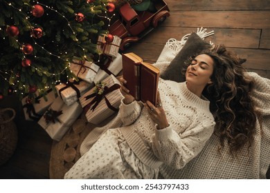 Young beautiful woman reading book, lying near Christmas tree in a cozy decorated room. - Powered by Shutterstock