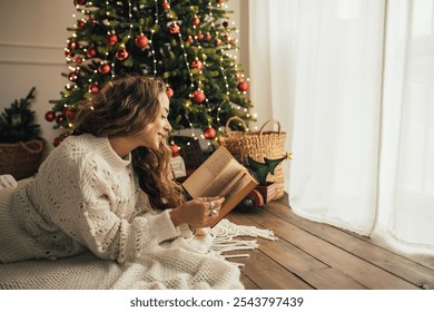 Young beautiful woman reading book, lying near Christmas tree in a cozy decorated room. - Powered by Shutterstock