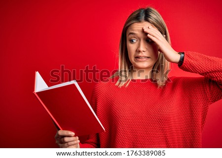 Young beautiful woman reading book standing over isolated red background stressed with hand on head, shocked with shame and surprise face, angry and frustrated. Fear and upset for mistake.