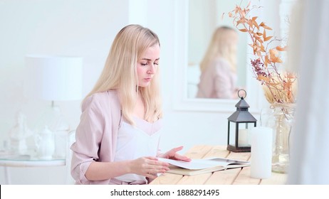 Young Beautiful Woman Reads A Book At The Table In The Living Room. Soft Focus. Selective Focus.