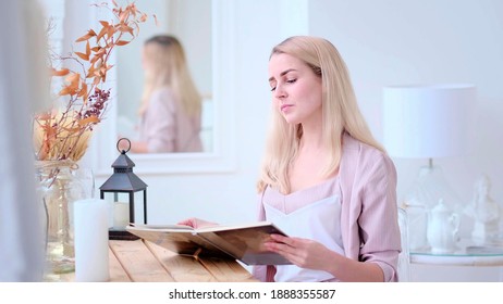 Young Beautiful Woman Reads A Book At The Table In The Living Room. Soft Focus. Selective Focus.