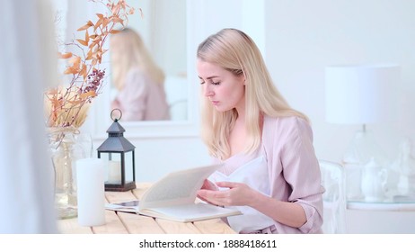 Young Beautiful Woman Reads A Book At The Table In The Living Room. Soft Focus. Selective Focus.