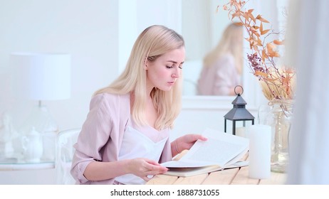 Young Beautiful Woman Reads A Book At The Table In The Living Room. Soft Focus. Selective Focus.