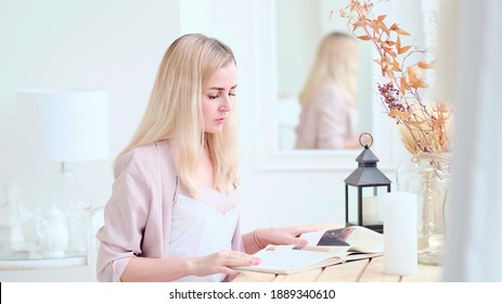 Young Beautiful Woman Reads A Book At The Table In The Living Room. Soft Focus. Selective Focus.