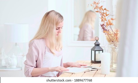 Young Beautiful Woman Reads A Book At The Table In The Living Room. Soft Focus. Selective Focus.