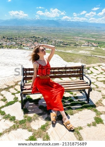 A young beautiful woman in a red dress walking in Pamukkale, Turkey, against the backdrop of the ruins of the ancient city of Hierapolis