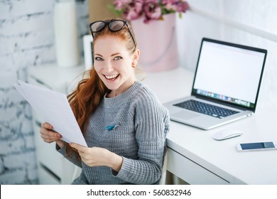 Young beautiful woman with red hair, wearing glasses, working in the office, uses a laptop and mobile phone - Powered by Shutterstock