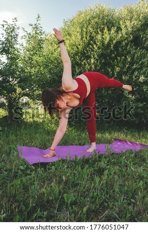 young beautiful woman in red leggings and a top practicing yoga in a city park 