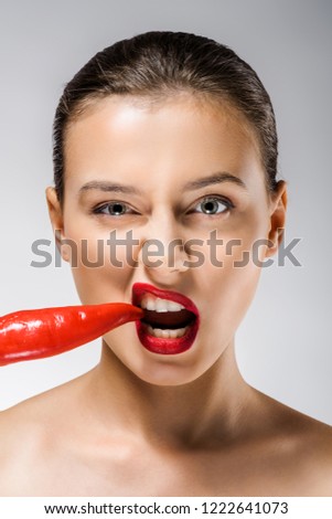 young beautiful woman with red lips biting chili pepper