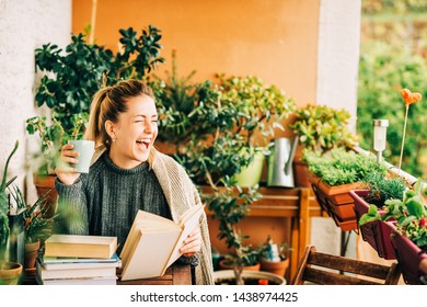 Young beautiful woman relaxing on cozy balcony, reading a book, wearing warm knitted pullover, holding cup of tea or coffee - Powered by Shutterstock