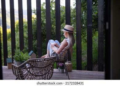 Young Beautiful Woman Relaxing On Cozy Terrace, Reading A Book, Digital Detox And Weekend Away Concept.