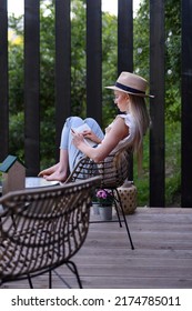 Young Beautiful Woman Relaxing On Cozy Terrace, Reading A Book, Digital Detox And Weekend Away Concept.