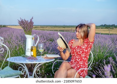 A Young Beautiful Woman Relaxing On A Nice Summer Afternoon, With A Good Book, And A Glass Of Wine In A Lavender Field.