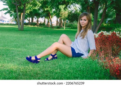 A Young Beautiful Woman Relaxing On A Green Lawn On A Bright Sunny Day. A Woman In A Public Park For Recreation In A Tropical Climate.