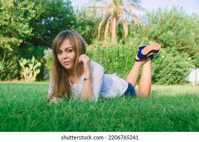 A Young Beautiful Woman Relaxing On A Green Lawn On A Bright Sunny Day. A Womanin A Public Park For Recreation In A Tropical Climate.