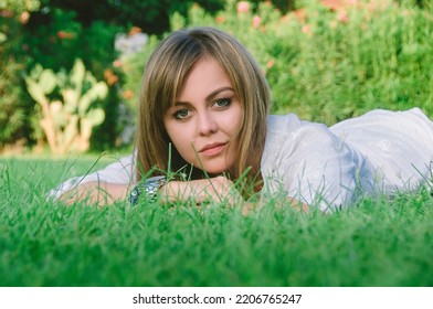 A Young Beautiful Woman Relaxing On A Green Lawn On A Bright Sunny Day. A Womanin A Public Park For Recreation In A Tropical Climate.