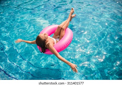 Young beautiful woman is relaxing in swimming pool with rubber ring.