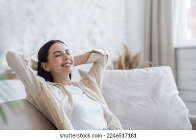 Young beautiful woman resting on sofa at home. She put her hands behind her head, closed her eyes. - Powered by Shutterstock