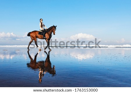 Young beautiful woman ride on sand beach. Horse with rider run along sea surf by water pool. Horseback walking tours, outdoor recreational sport, adventure activity on family summer vacation with kids