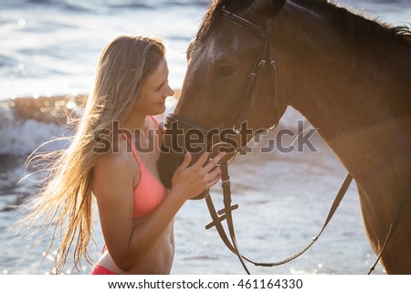 Young beautiful woman ride walk and pose with her horse on the river sunset background sun beams strong back light