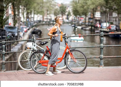 Young beautiful woman riding a bicycle on the bridge over the water channel in Amsterdam old city - Powered by Shutterstock