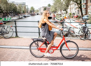 Young beautiful woman riding a bicycle on the bridge over the water channel in Amsterdam old city