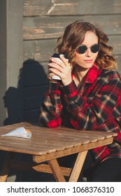 Young Beautiful Woman In Round Glasses And In Flannel Shirt Drinking Coffee