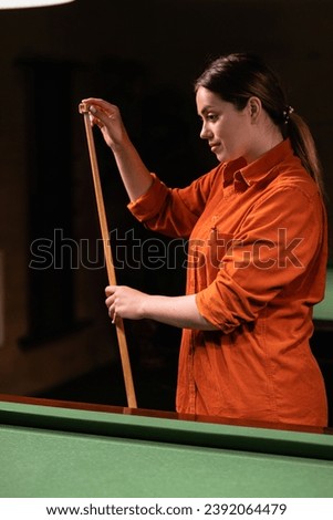 Young beautiful woman rubs the tip of a billiard cue with chalk for a more accurate shot. Girl prepares to play billiards by rubbing his cue with chalk. Copy space