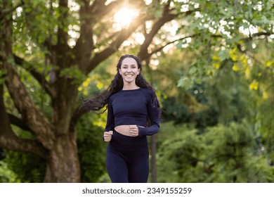 Young beautiful woman running in the park, portrait of a Latin American woman jogging and doing active exercises, sportswoman smiling and looking at the camera among the trees. - Powered by Shutterstock