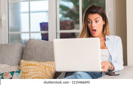 Young Beautiful Woman With Shock Face Using Laptop On The Sofa Looking Susprised.