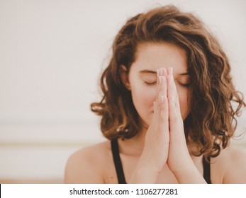 Young beautiful woman with short curly hair meditating in light fitness studio. Hands in namaste. Pray, gratitude, yoga, love God concept. - Shutterstock ID 1106277281