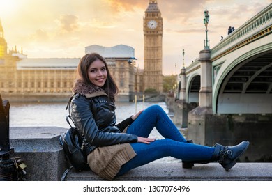 Young, beautiful woman sits in front of the Big Ben in London, Westminster, during sunset time; student city traveler is exploring Europe