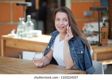 Young beautiful woman sitting in cafe, drinking water and coffee and speaking on a phone .   - Shutterstock ID 1103224337