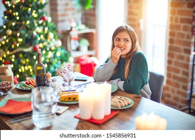 Young Beautiful Woman Sitting Eating Food Around Christmas Tree At Home Looking Stressed And Nervous With Hands On Mouth Biting Nails. Anxiety Problem.