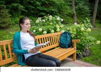 Young beautiful woman sitting on a bench and reading a book in the park. Cute girl outdoors on a summer day. - Shutterstock ID 1460665658