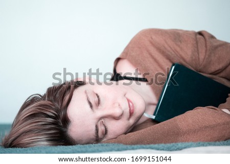 Young beautiful woman sleeping dreamily hugging a book on a white background. Side view