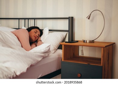 Young beautiful woman sleeping in her bed at home with a smartphone next to her on a nightstand