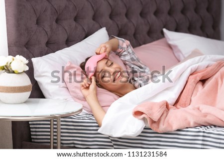 Young beautiful woman with sleeping mask waking up in morning at home