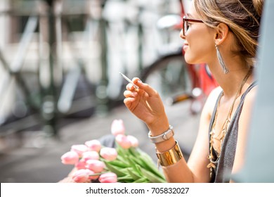Young beautiful woman smoking a cigarette sitting with flowers in Amsterdam city