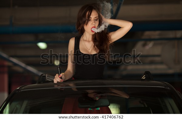 Young beautiful woman smoking ( vaping ) e-cigarette
with smoke in car luke