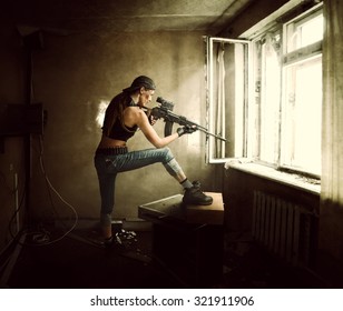 Young beautiful woman sniper and Soldier aiming a rifle at the window. She is in old room of abandoned building