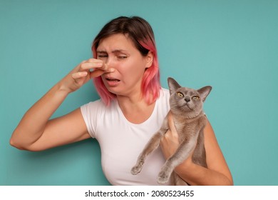 Young beautiful woman standing against blue background, holding her nose because of a bad smell coming out from the cat. - Shutterstock ID 2080523455